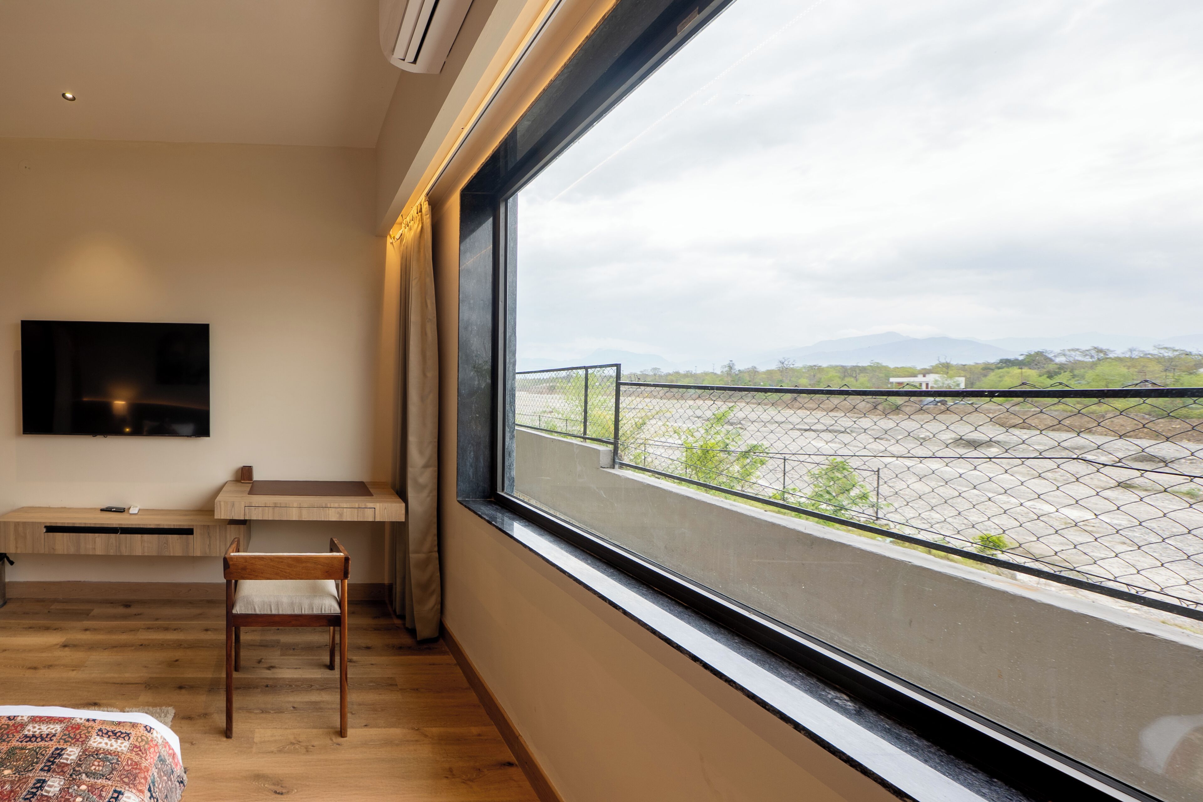 Una habitación moderna con un ventanal grande, una cama, un escritorio y un televisor montado en la pared.