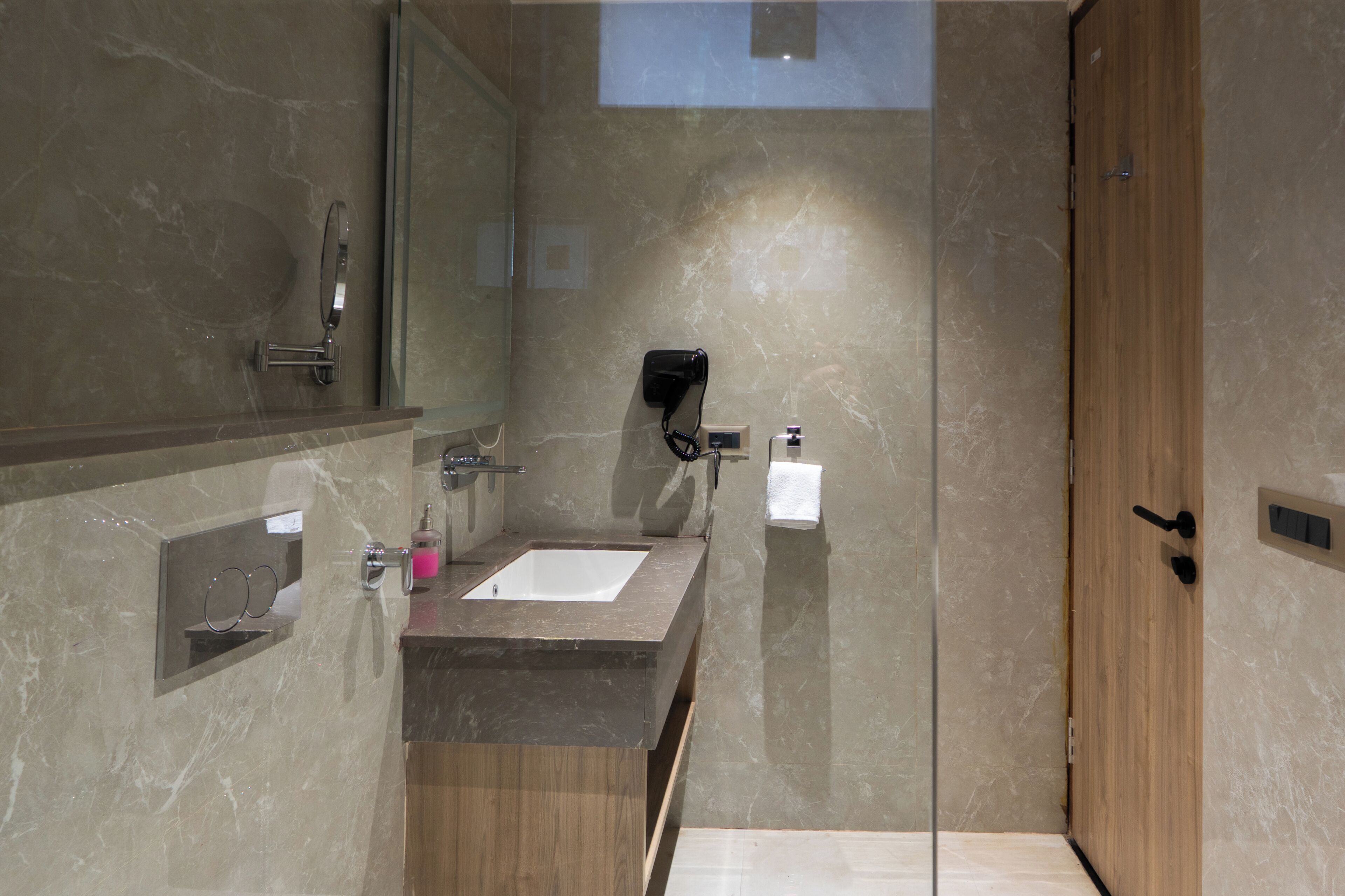 A modern bathroom with a marble vanity, a glass shower enclosure, and a wooden door.