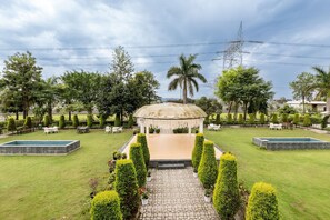 A gazebo with a tiled floor, surrounded by a well-manicured lawn, a stone pathway, and a small pool. - juSTa Nature's Nest Resort  (Rishikesh)