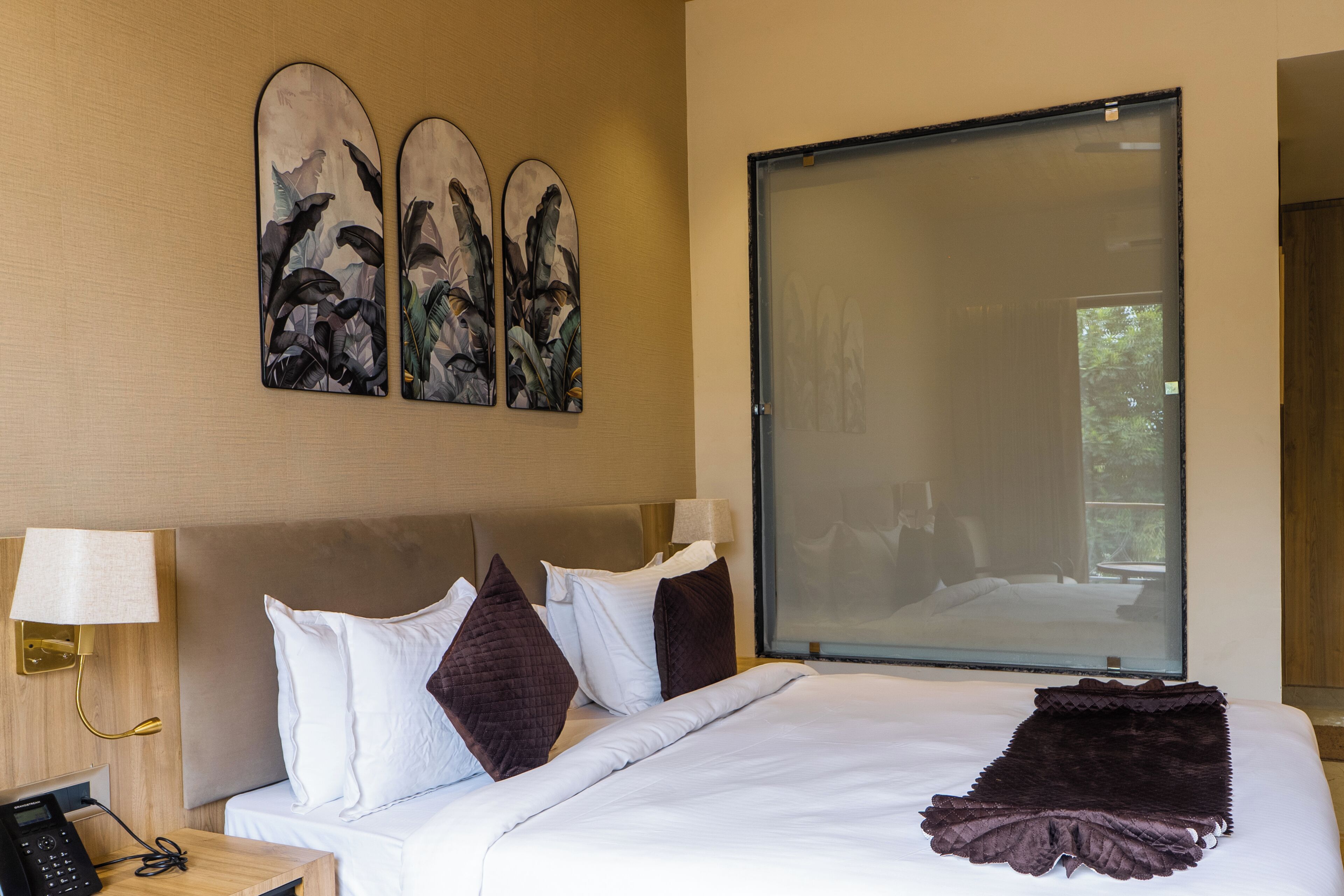 Ein Hotelzimmer mit einem Bett, einem Nachttisch mit Telefon, einer Wandlampe und einem großen Fenster.