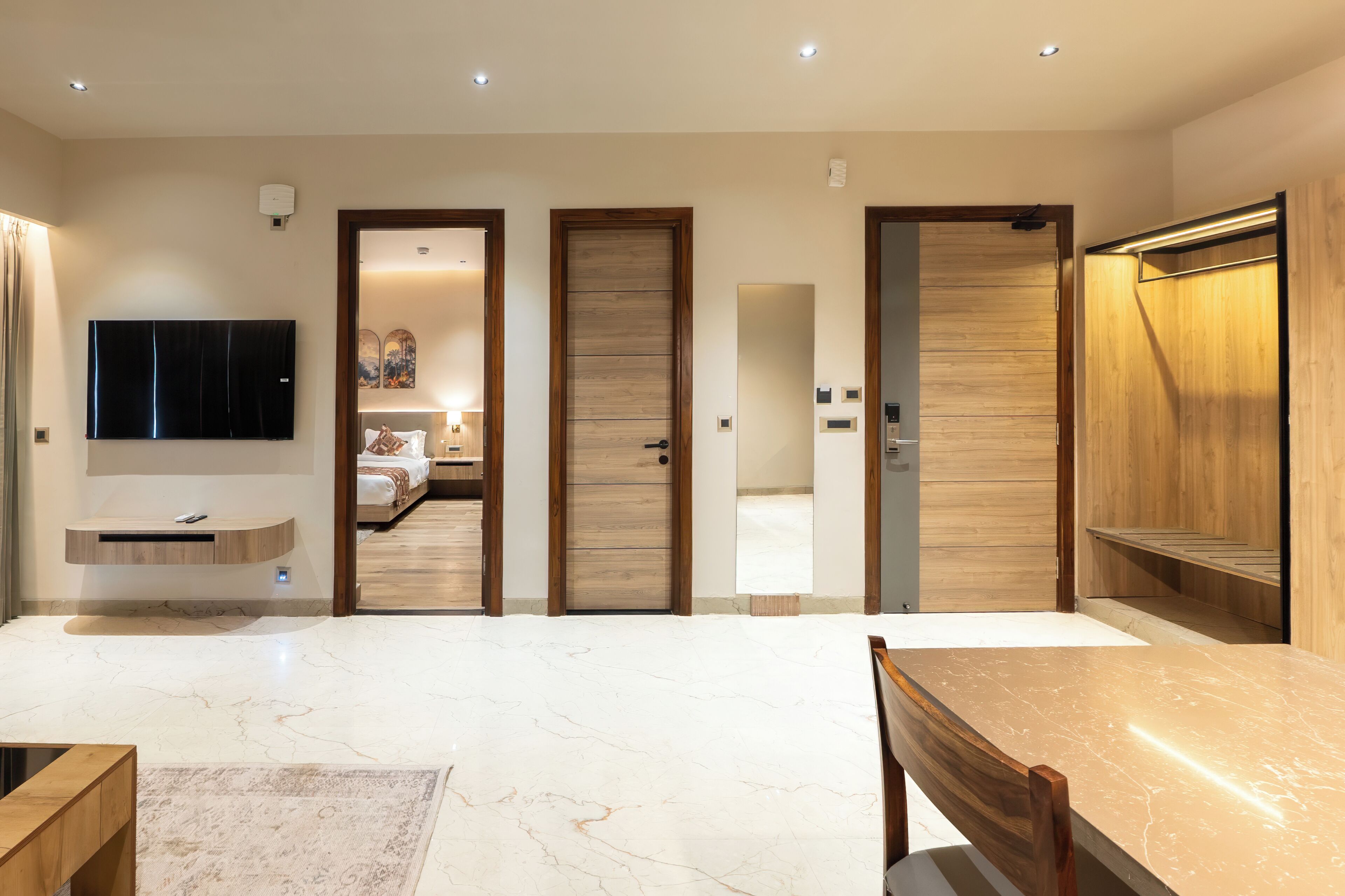 Habitación de hotel moderna con piso de mármol, televisor de pantalla plana, puertas de madera y un banco integrado.