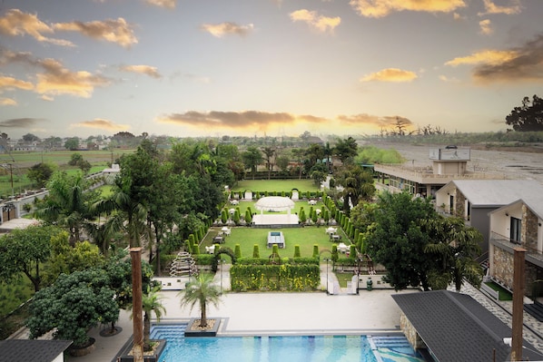 A resort with a swimming pool, manicured lawn, and a view of the surrounding countryside. - juSTa Nature's Nest Resort (Rishikesh)