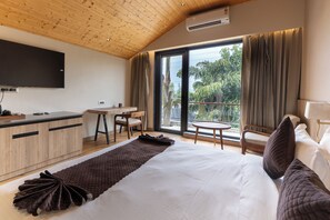 Une chambre d’hôtel moderne avec un plafond en bois, un téléviseur à écran plat, un coin repas, un balcon avec des rideaux et un grand lit avec des oreillers.