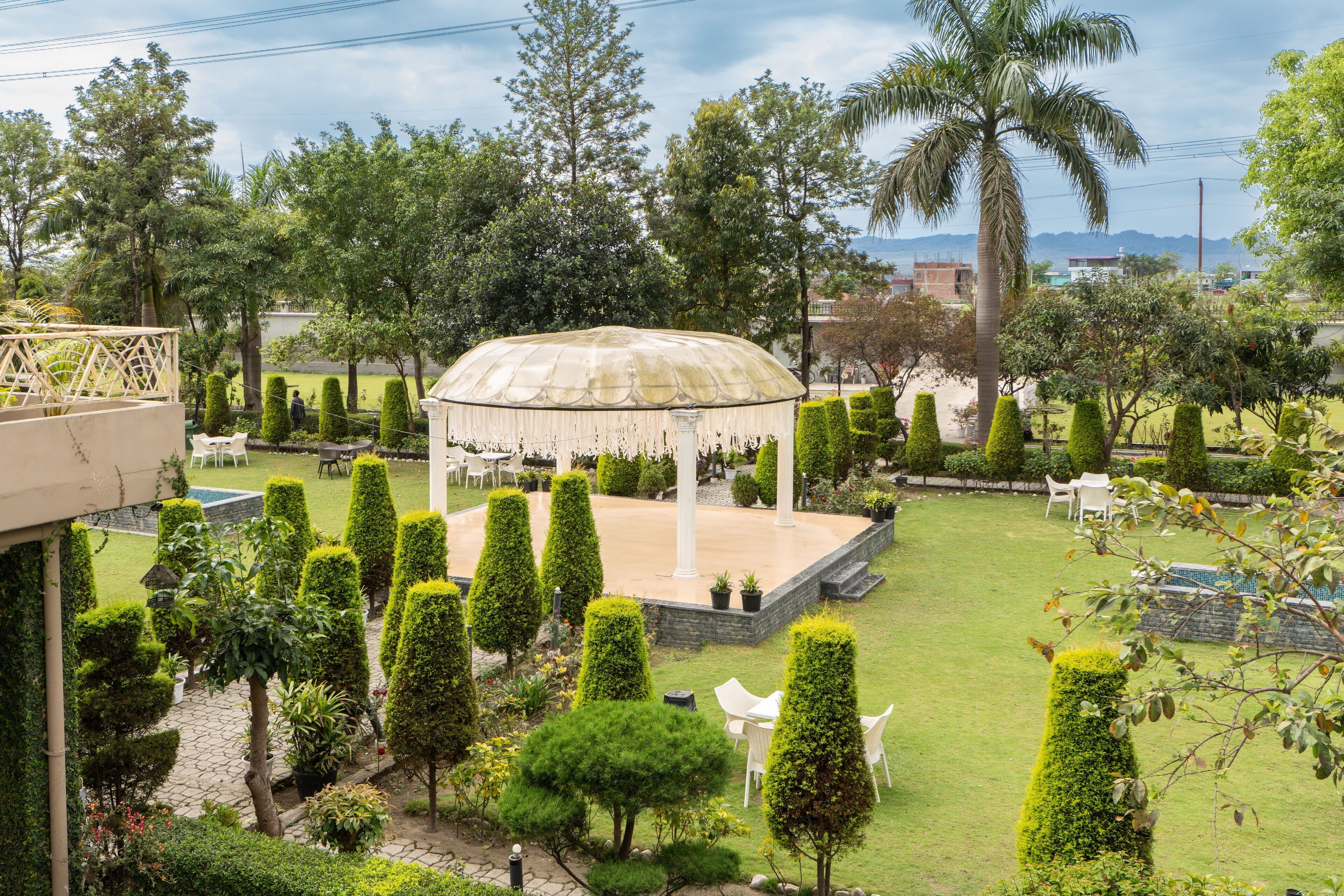 Un jardín con un pabellón, setos podados y una palmera.