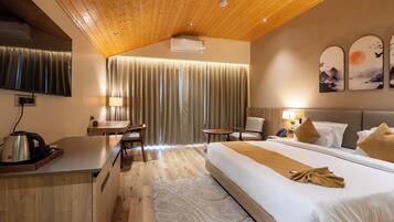 Habitación de hotel con techo de madera, cama con manta color beige, escritorio con hervidor, una silla, una mesita y televisor montado en la pared.