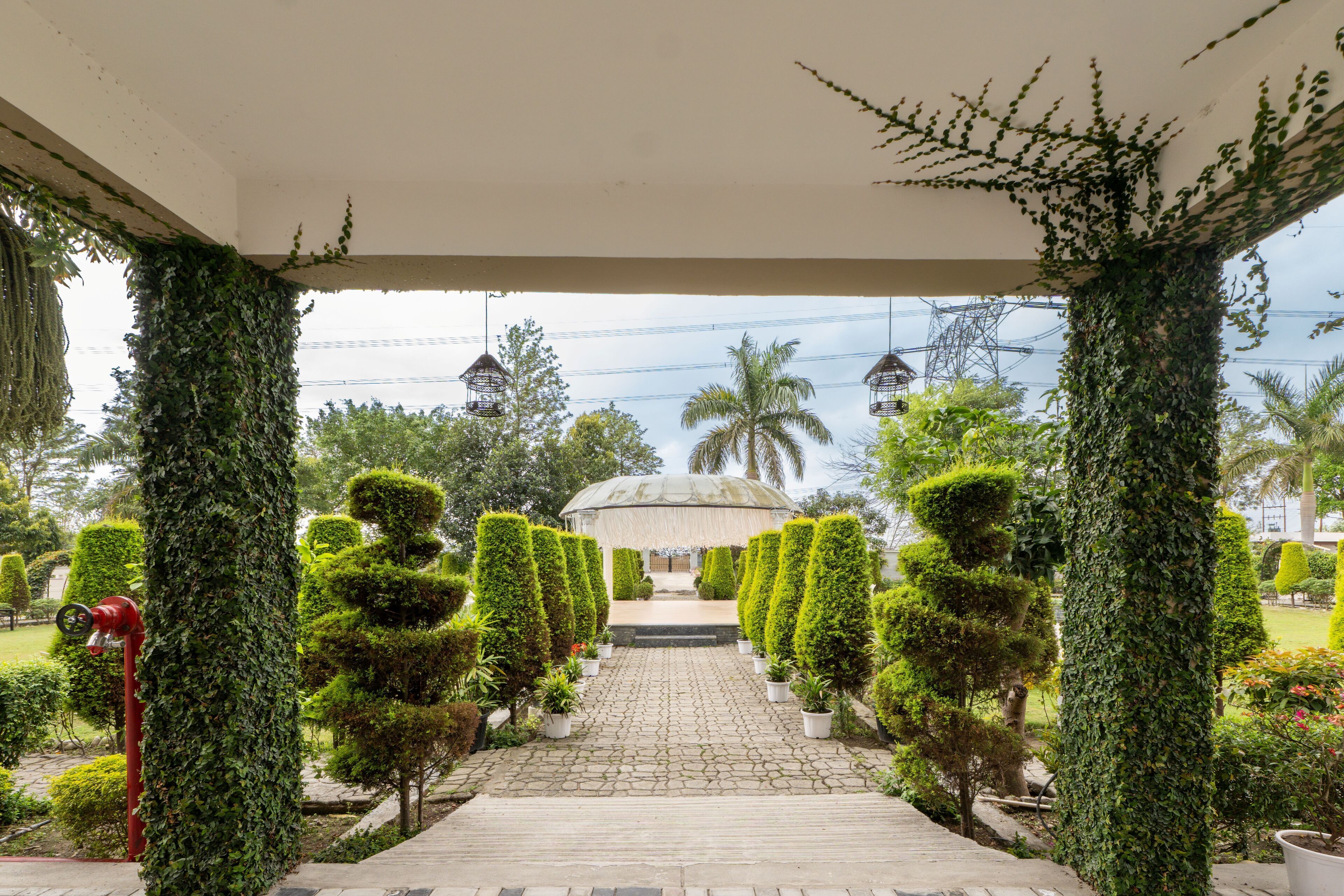 A paved pathway leading to a covered area with a dome structure, surrounded by neatly trimmed hedges and potted plants.