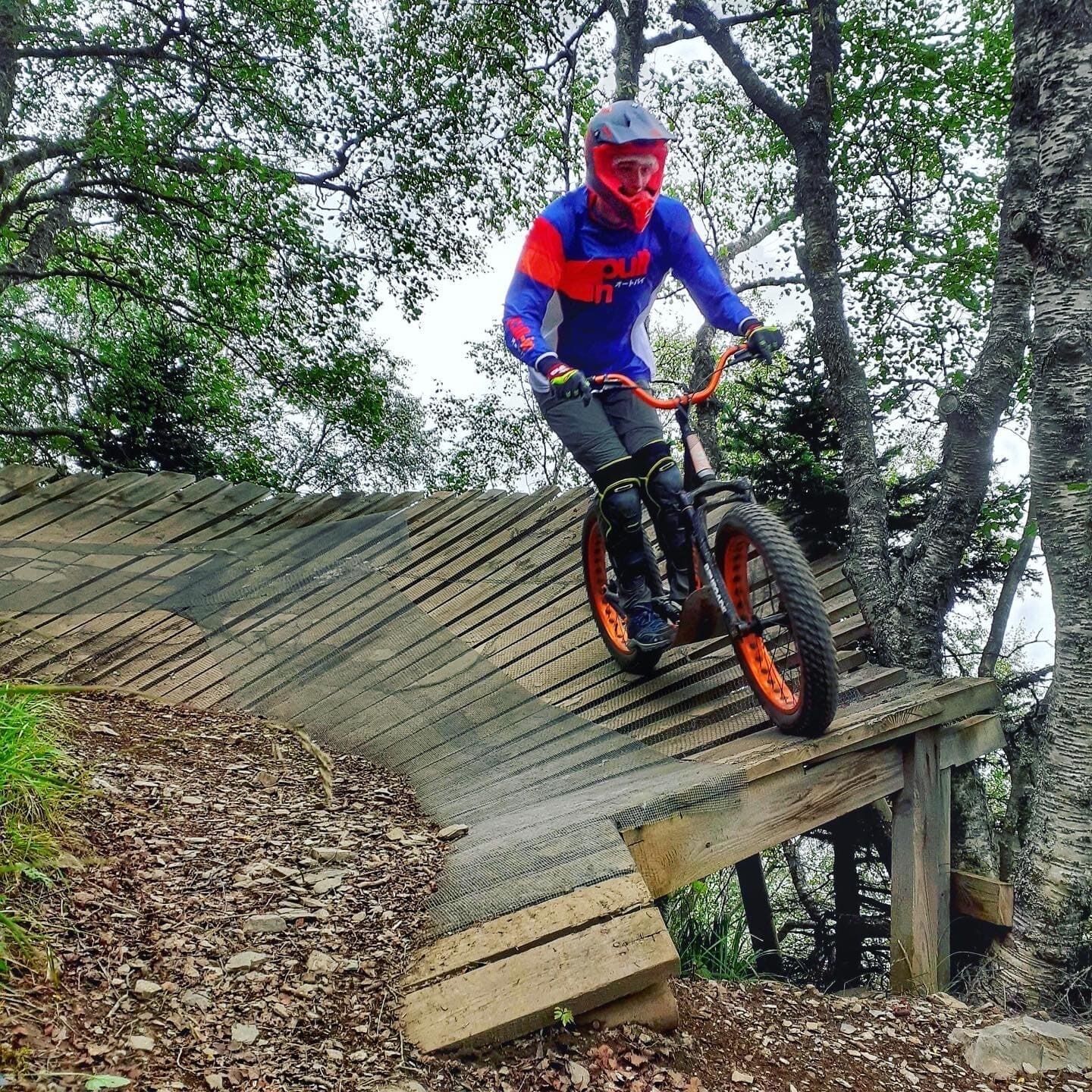 A person riding a mountain bike on a wooden bridge in a wooded area.
