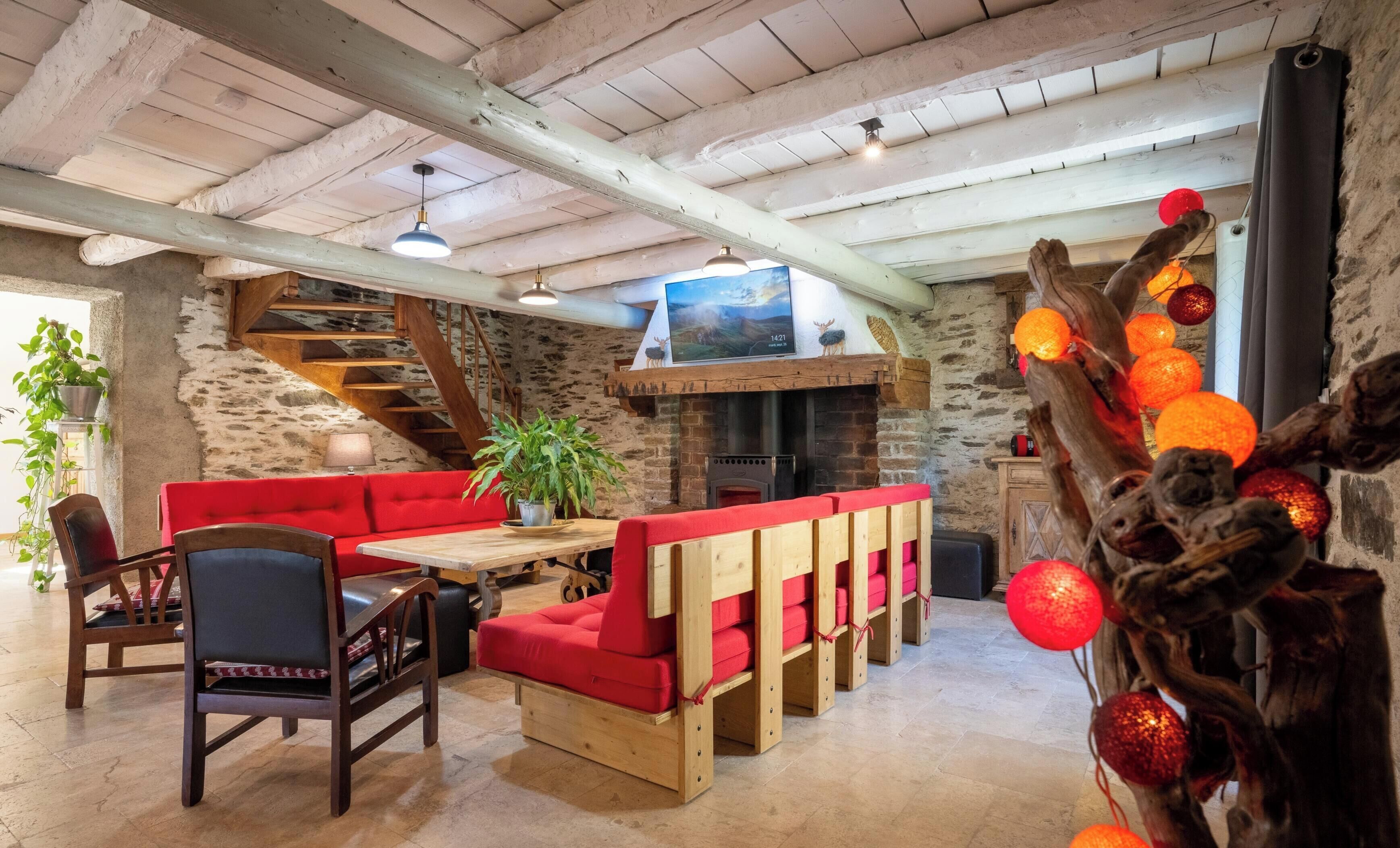 A rustic interior with a stone wall, wooden staircase, red seating, and a fireplace.