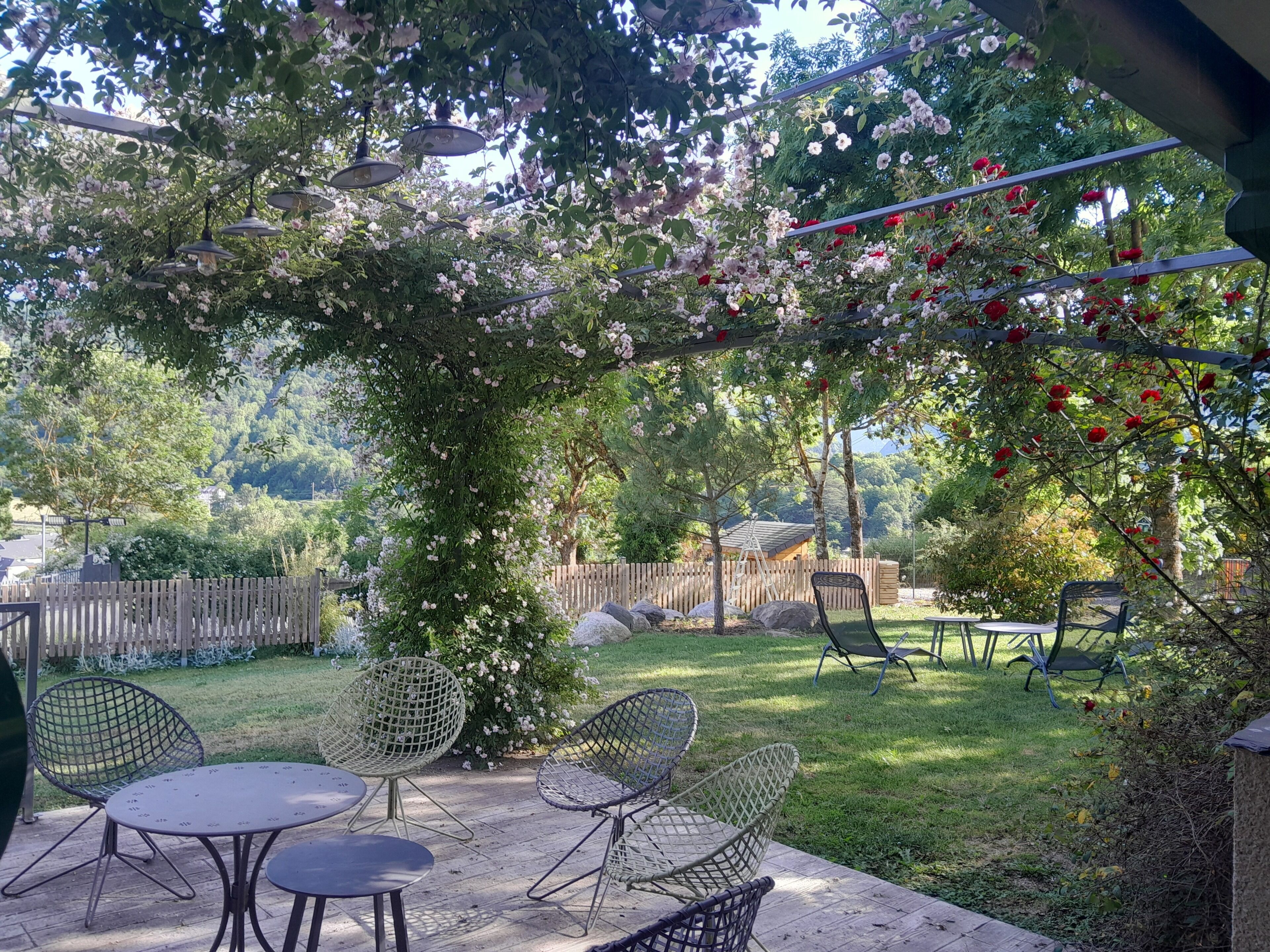 An outdoor patio with a pergola covered in flowers, a wooden fence, and outdoor furniture.