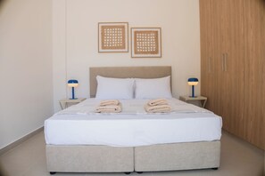 Ein ordentlich gemachtes Bett mit zwei Kissen und zwei gefalteten Handtüchern, ein Kopfteil, zwei Nachttische mit Lampen sowie zwei gerahmte Bilder an der Wand.