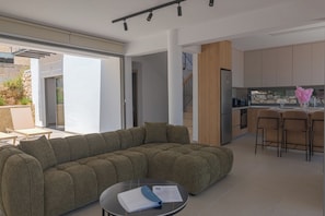 Ein modernes Wohnzimmer mit einer Eckcouch, einem Essbereich mit Barhocker und einer Küche mit Holzschränken.