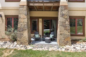 A house with a stone facade, a covered patio with outdoor furniture, and a view of the surrounding landscape. - Steps from Slopes | Winter Shuttle | Pool & Hot Tub (Steamboat Springs)