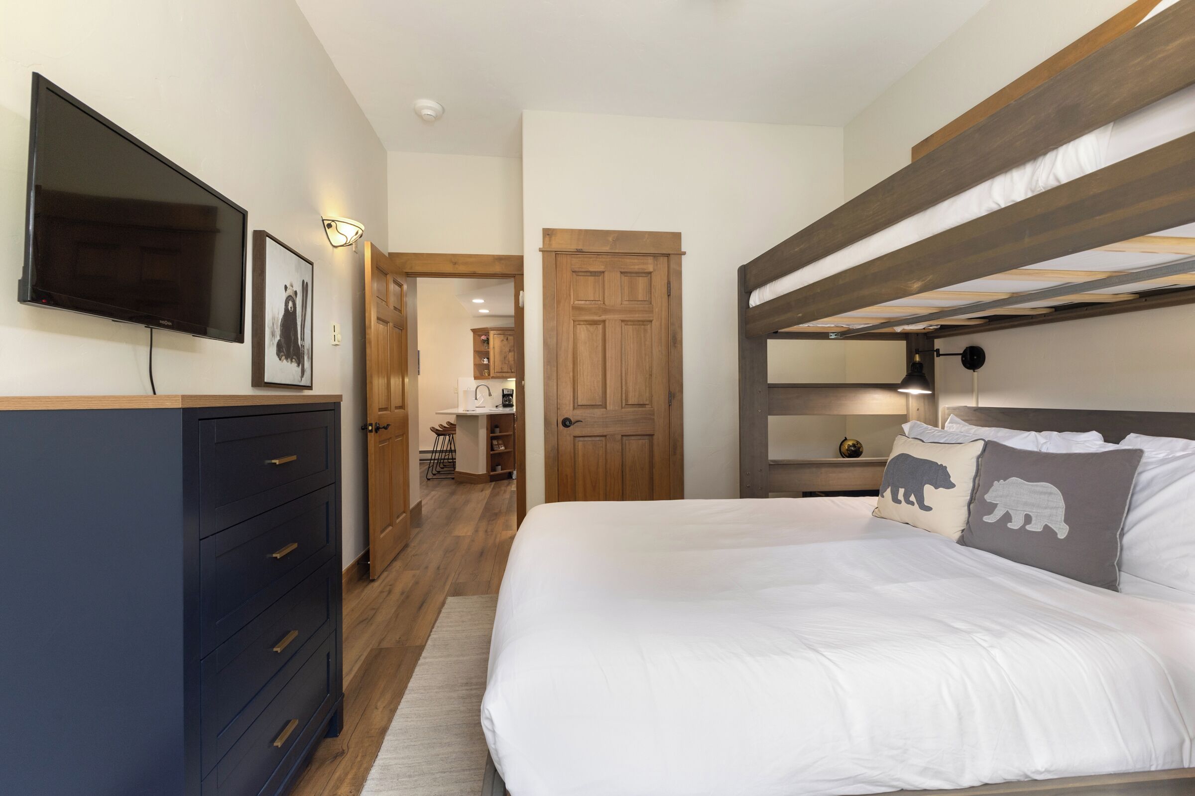 Une chambre avec un lit superposé, une télévision, une commode et une porte donnant sur la cuisine.