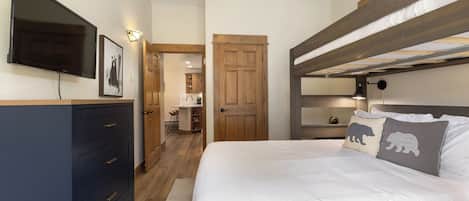 Une chambre avec un lit superposé, une télévision, une commode et une porte donnant sur la cuisine.