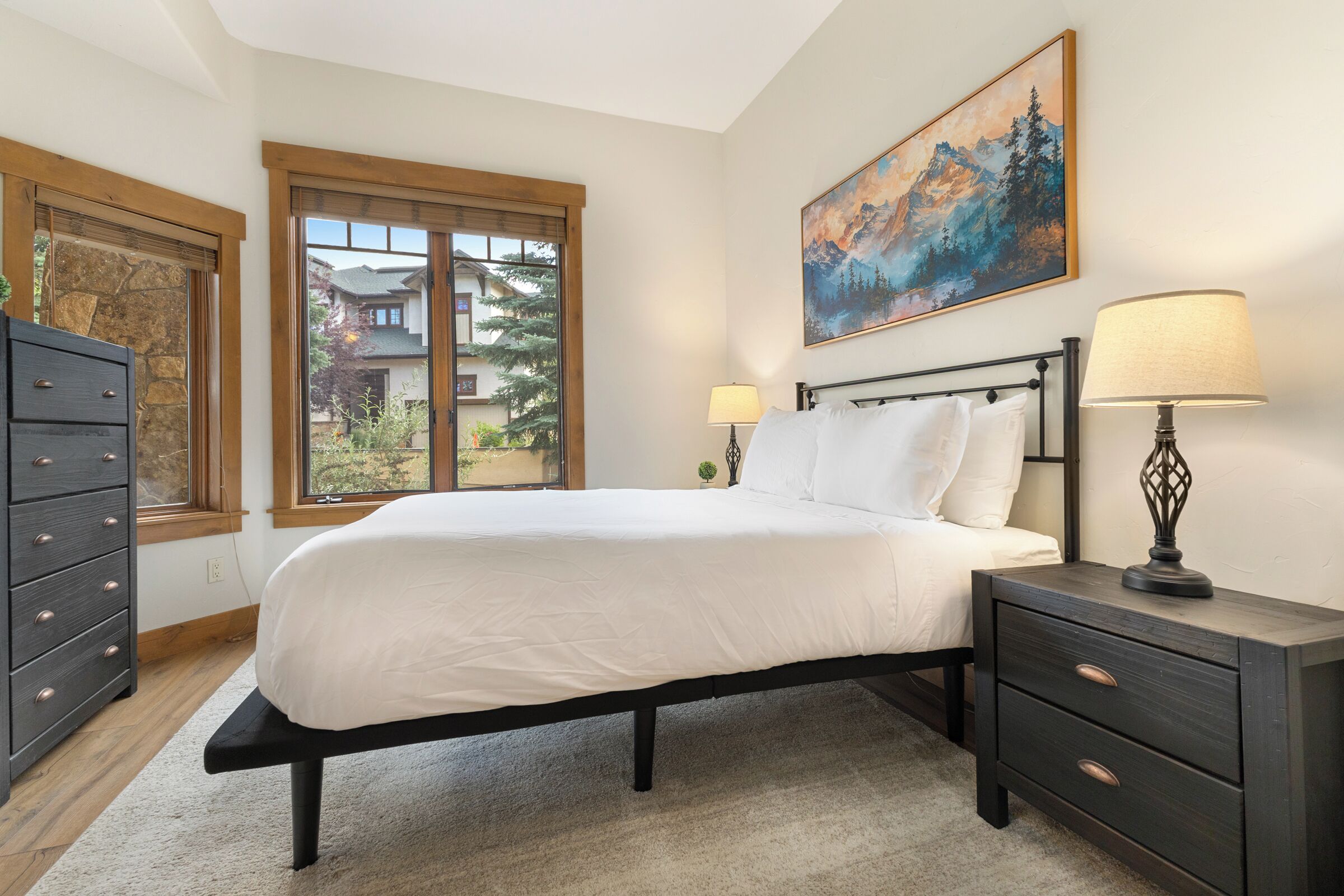 A bedroom with a bed, bedside tables, a dresser, a window, and a painting on the wall.