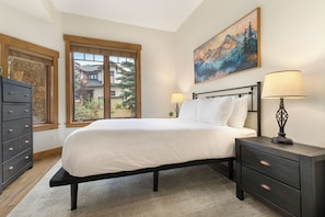 Une chambre à coucher avec un lit, des tables de chevet, une commode, une fenêtre et un tableau au mur.