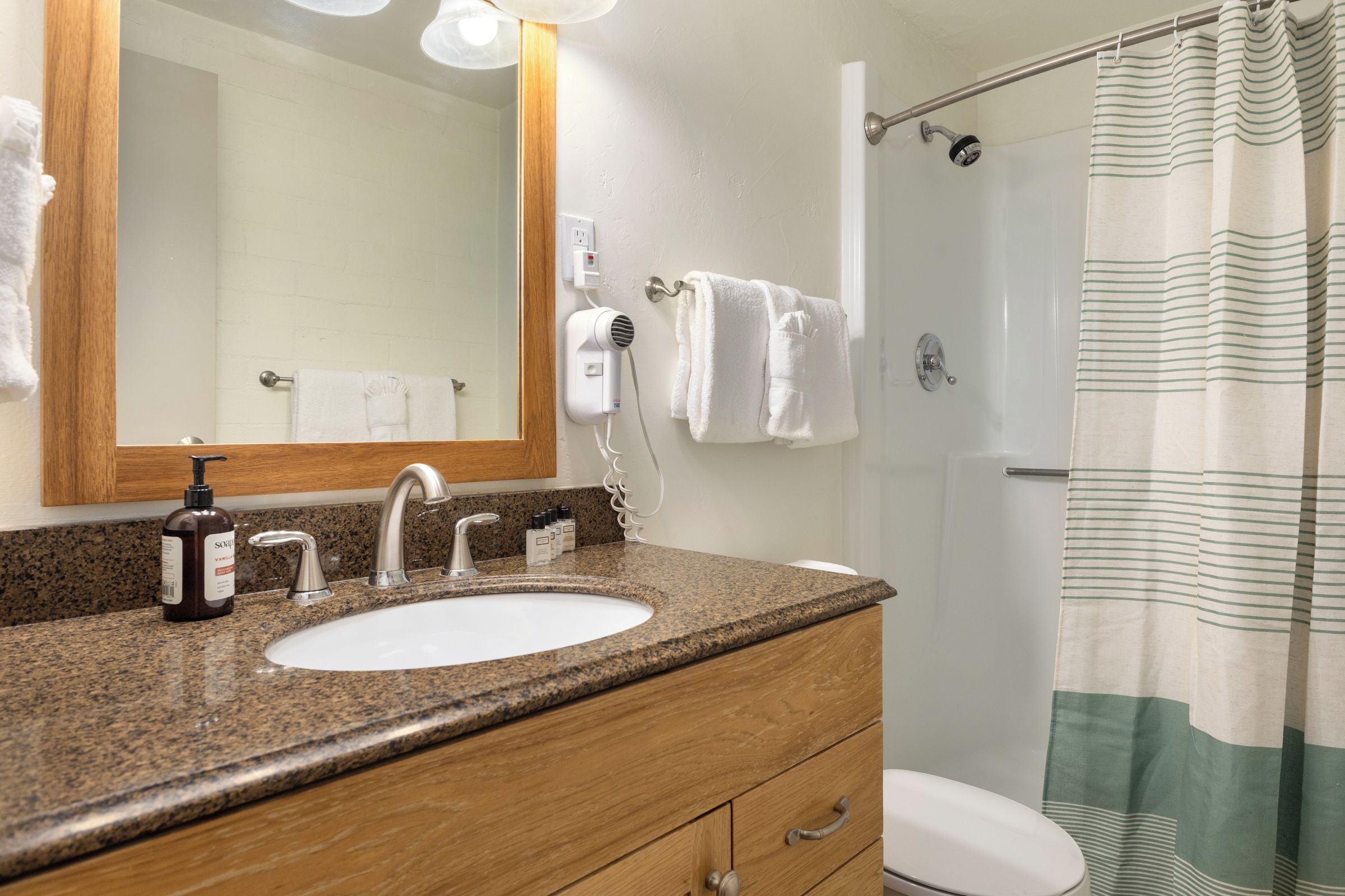A bathroom with a granite countertop, a white sink, a mirror, a towel rack, a shower curtain, and a toilet.