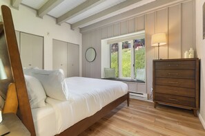 Une chambre à coucher avec un lit en bois, une commode, une fenêtre donnant sur un beau paysage et un miroir fixé au mur.