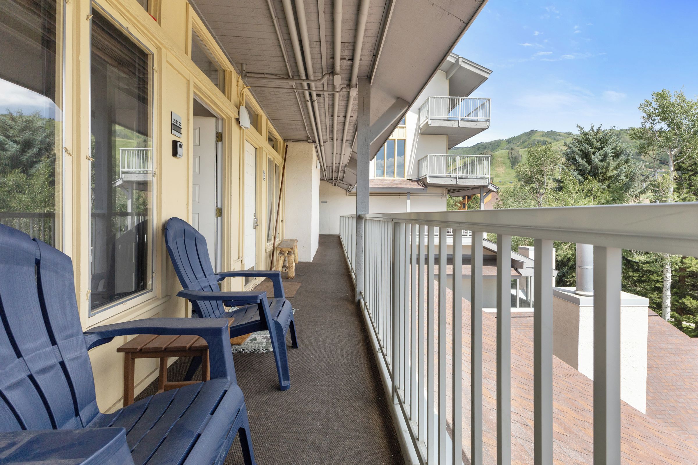 Un balcon avec deux fauteuils Adirondack bleus, une table en bois et une vue sur un paysage vallonné.