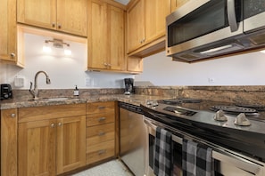 A kitchen with wooden cabinets, a stainless steel stove, a microwave, and a dishwasher. - Slopeside | Hot Tub | Bonus Den with Video Games (Steamboat Springs)