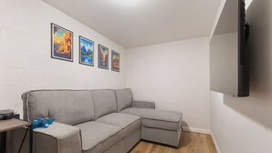Un saló modern amb un sofà seccional gris, un televisor de pantalla plana muntat a la paret i tres quadres enmarcats a la paret.