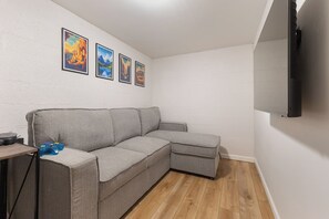 Ein modernes Wohnzimmer mit einem grauen Ecksofa, einem flachbildfernseher an der Wand und drei gerahmten Postern an der Wand.