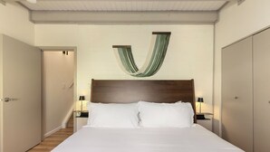 Habitació d'hotel amb un llit gran, dues taules de nit amb làmpades, un capçal de llit de fusta i una decoració penjant de tela verda i blanca.