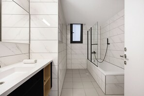 A modern bathroom with a white marble tile design, a glass-enclosed shower, a white bathtub, and a small window. - Spacious 4BR Apt l Sunny Balcony & Mamad (Rishon LeTsiyon)