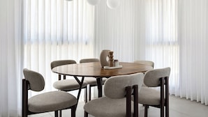A dining area with a round wooden table, six upholstered chairs, and three pendant lights. - Spacious 4BR Apt l Sunny Balcony & Mamad (Bat Yam)