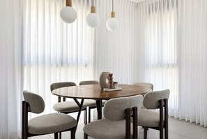A dining area with a round wooden table, six upholstered chairs, and three pendant lights. - Spacious 4BR Apt l Sunny Balcony & Mamad (Bat Yam)