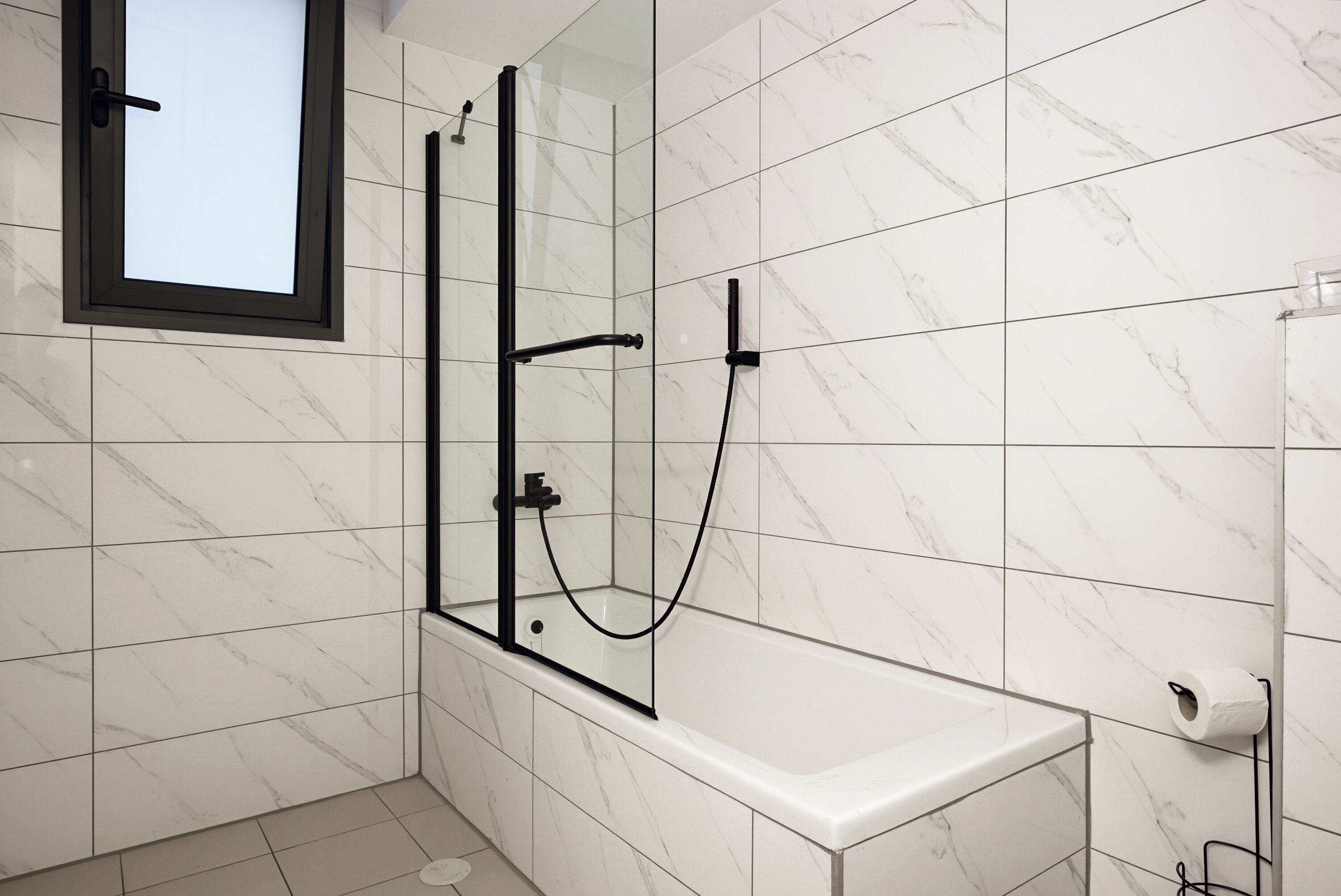Un baño moderno con cabina de ducha de vidrio, azulejos de mármol blanco y lavamanos blanco.