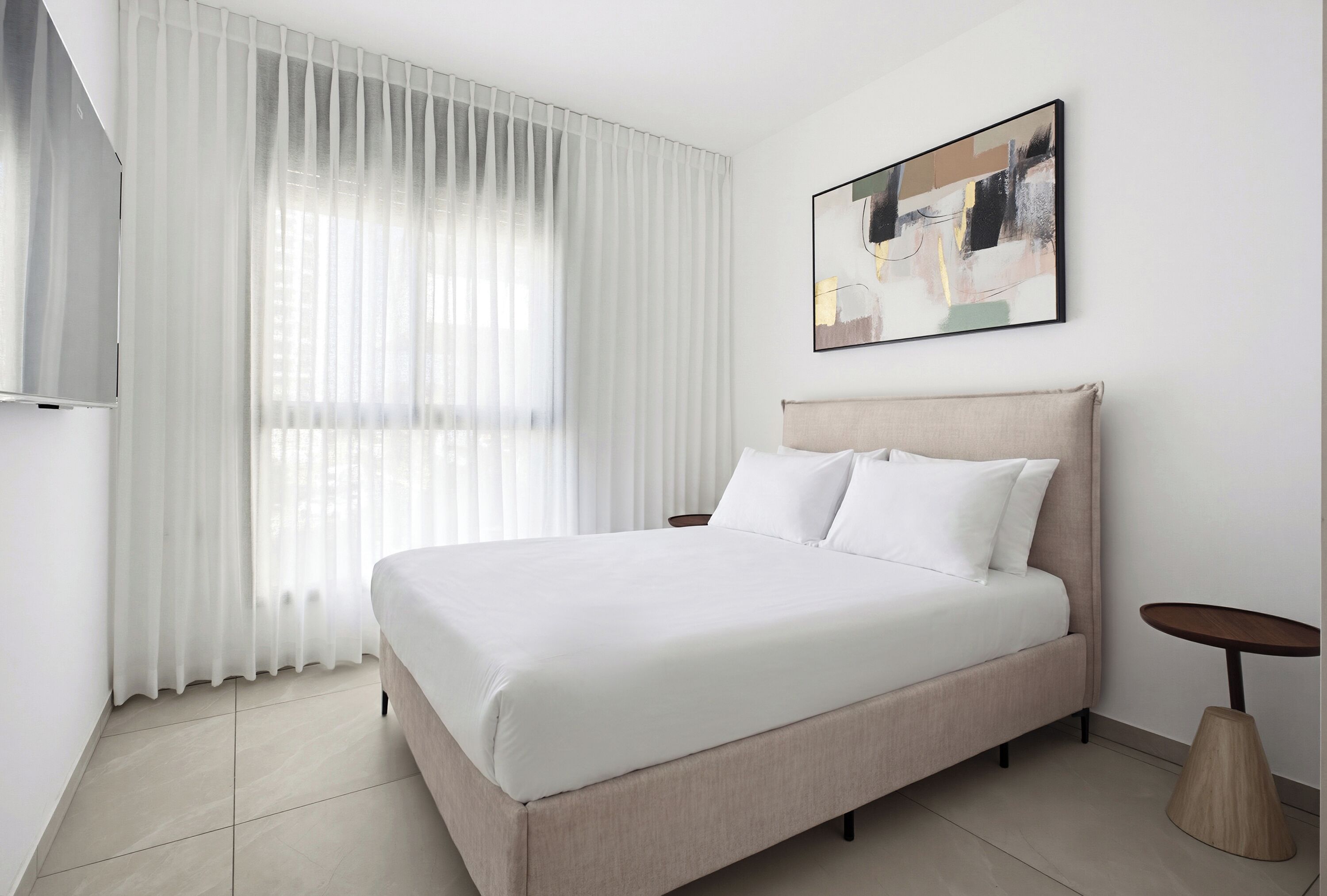 A hotel room with a bed, a painting on the wall, and a small table.
