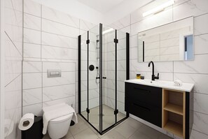 A modern bathroom with a glass-enclosed shower, a white toilet, and a black vanity with a mirror. - Spacious 4BR Apt l Sunny Balcony & Mamad (Bat Yam)