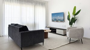 A modern living room with a sofa, armchair, coffee table, and a TV on a stand. - Spacious 4BR Apt l Sunny Balcony & Mamad (Bat Yam)