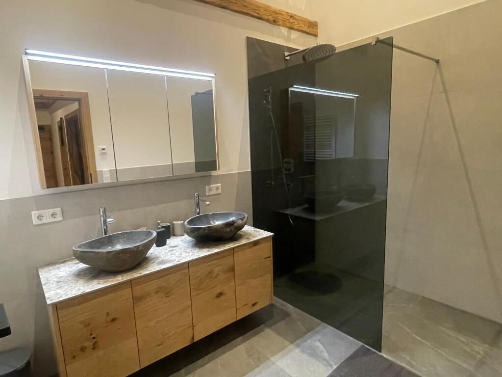 Une salle de bain moderne avec un meuble-lavabo en bois, deux vasques, un grand miroir et une douche à parois de verre.