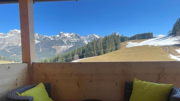 Un balcón de madera con dos sillas de mimbre, cada una con un cojín, con vistas a un paisaje montañoso.