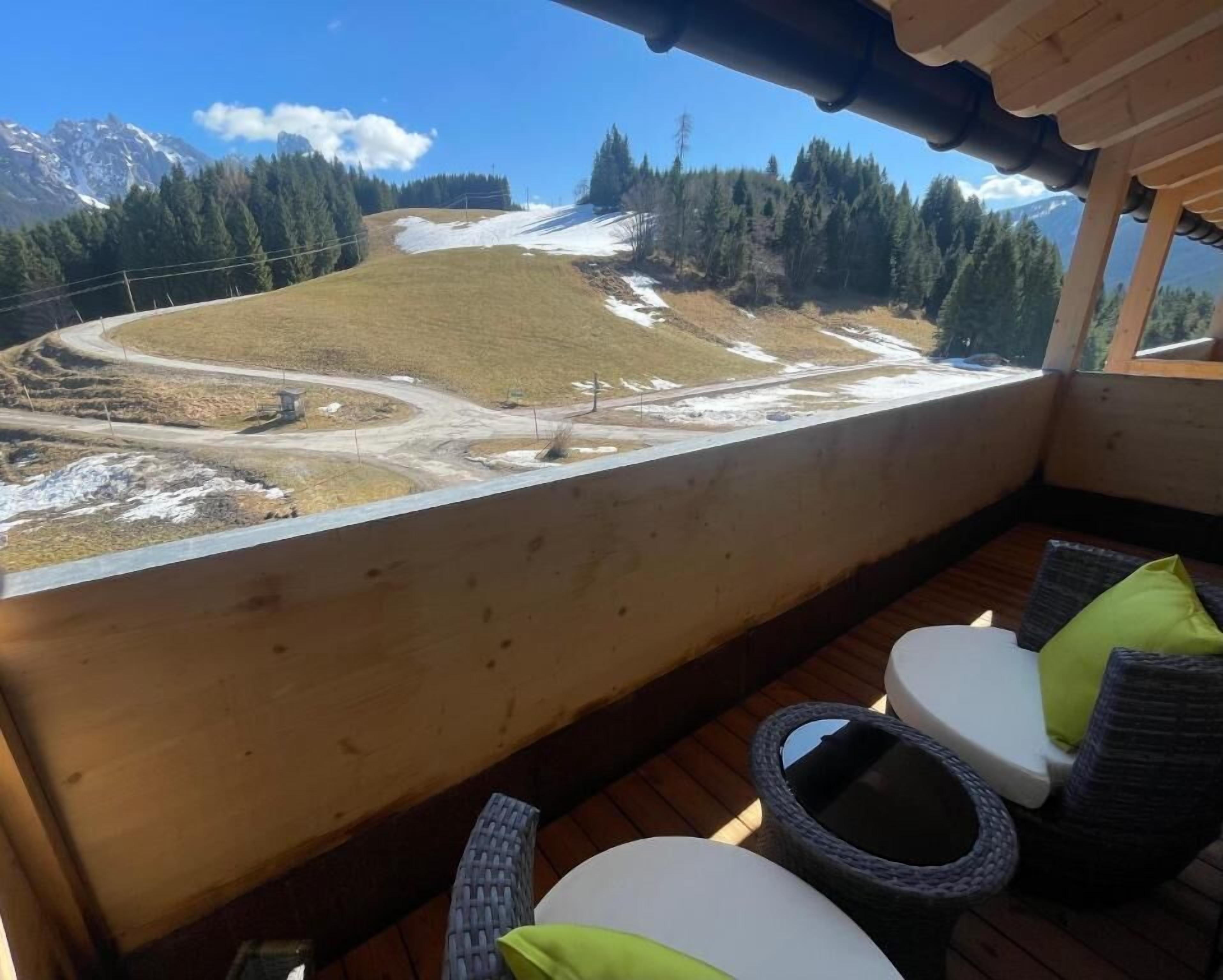 Een houten terras met zitplaatsen buiten, een sneeuwbedekte heuvel in de verte en een heldere lucht.