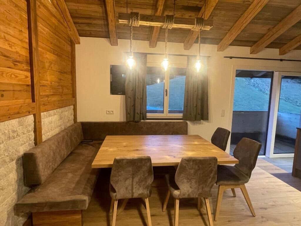 A wooden dining area with a bench and chairs, a large window with curtains, and a view of a snowy landscape.