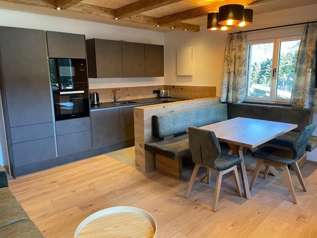 A modern kitchen with built-in appliances, a dining area with a bench, and a window with curtains.