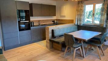 A modern kitchen with built-in appliances, a dining area with a bench, and a window with curtains.