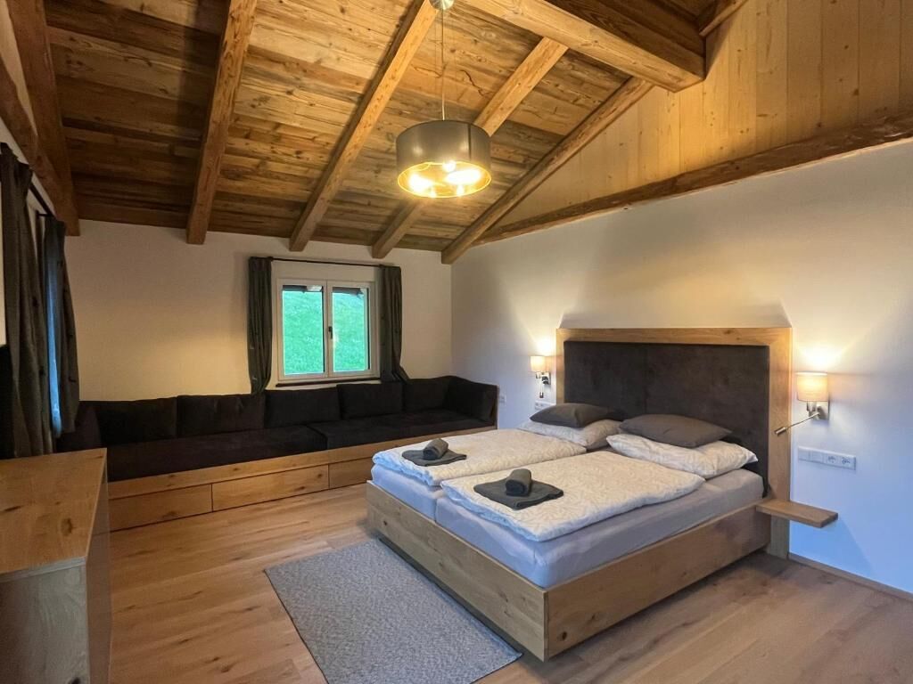 Une chambre avec un plafond en bois, un lit avec deux oreillers, un banc et une fenêtre.