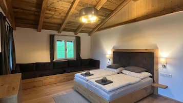 A bedroom with a wooden ceiling, a bed with two pillows, a bench, and a window.