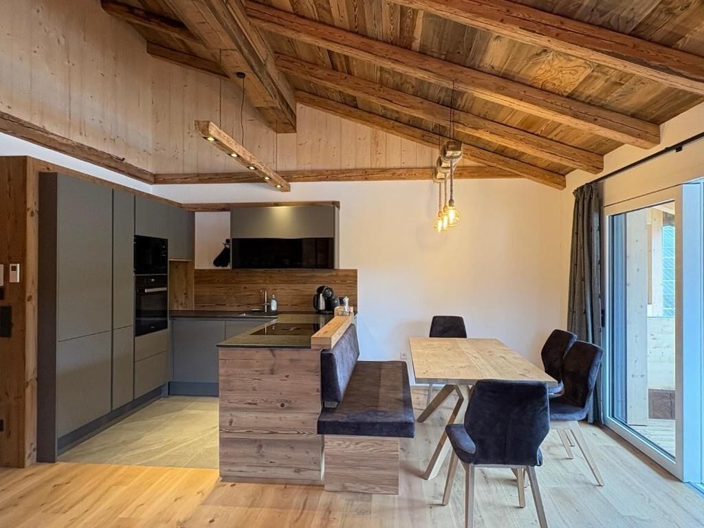 A modern kitchen with wooden beams, a dining area with a bench, and a large window.