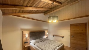 Un dormitorio con techo de madera, una cama con cabecera, una mesita de noche con lámpara y una puerta de madera.