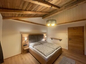 Ein Schlafzimmer mit Holzboden, einem Bett mit Kopfteil, einem Nachttisch mit Lampe und einer Holztür.