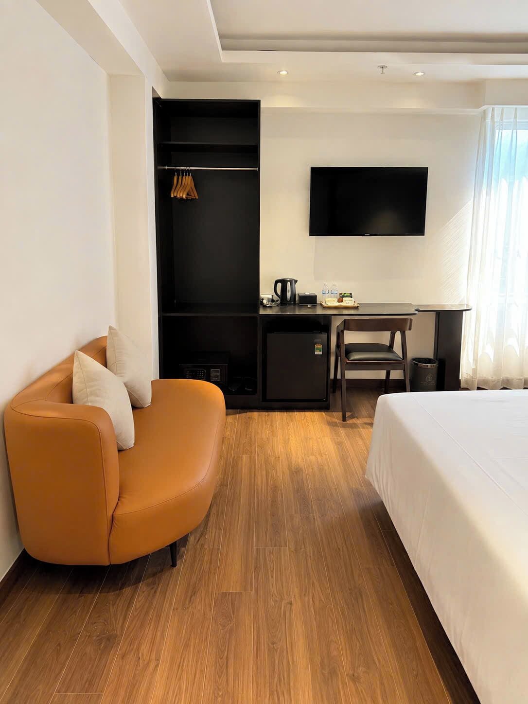 A hotel room with a bed, a sofa, a desk with a flat-screen TV, a coffee maker, and a wardrobe.