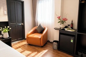 A hotel room with a brown leather chair, a small table with a vase of flowers, a minibar, and a trash can. - Corner Inn Ben Thanh Hotel (Ho Chi Minh City)