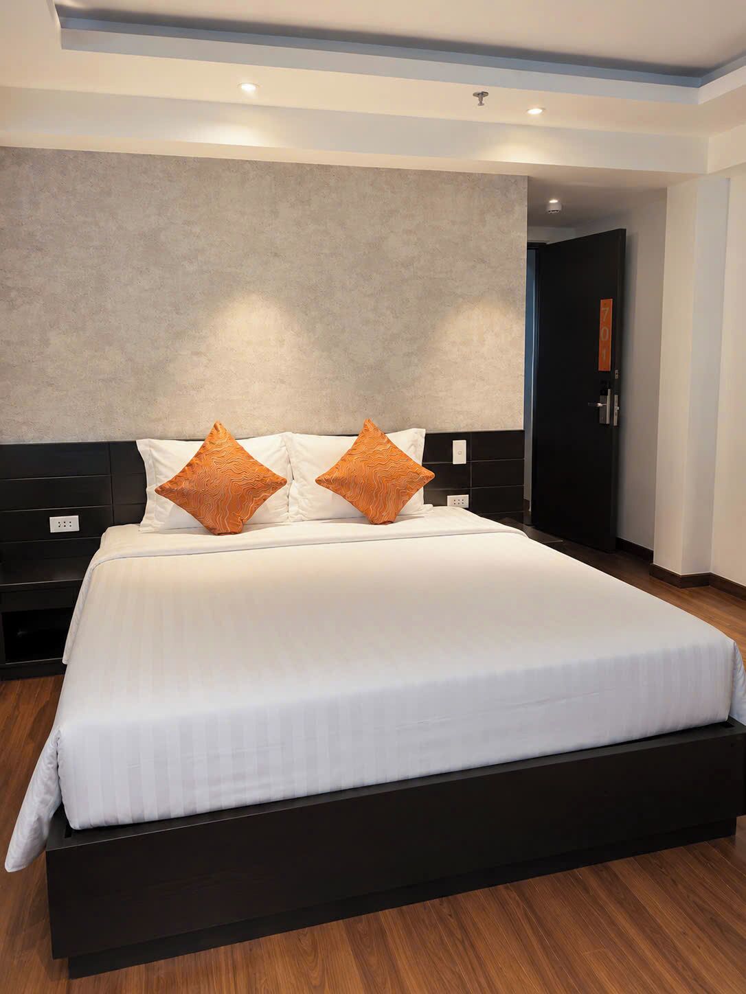 Moderni hotellihuone, jossa on suuri sänky, tumma puinen pääty ja neutraalin sävyinen seinä.