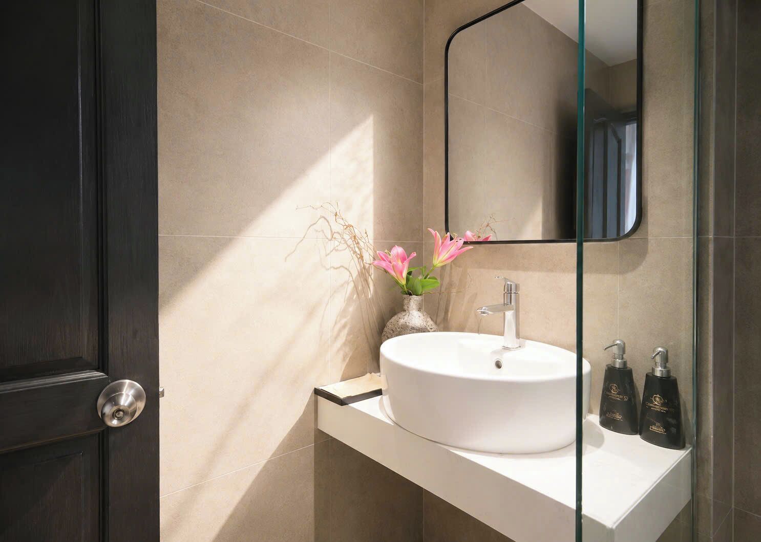 Ein Badezimmer mit einem weißen Waschbecken, einem Glasspiegel und einer Vase mit Blumen.
