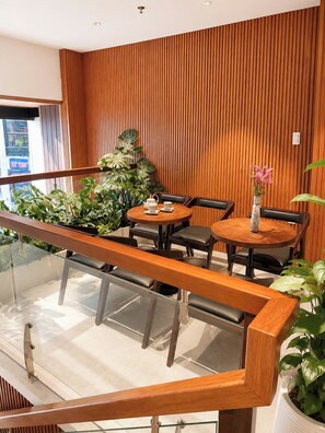 A modern indoor seating area with wooden panel walls, a glass railing, and potted plants. - Corner Inn Ben Thanh Hotel (Ho Chi Minh City)